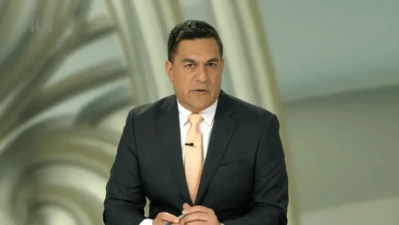 Julian WIlcox wearing a black suit, white shirt, and rose gold tie.
