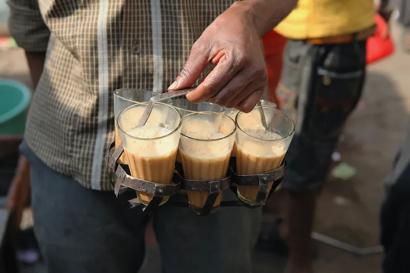 A chai vendor carrying glasses of tea.