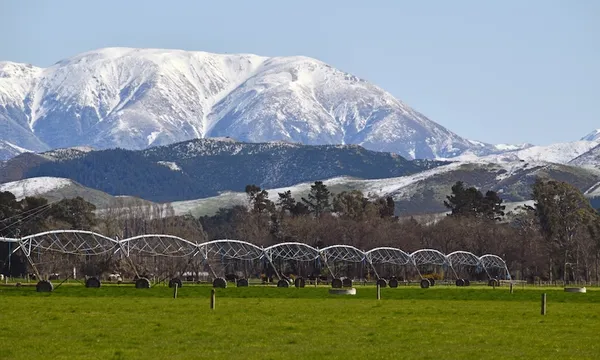 snowy mountains with big irrigators in a field in the foreground