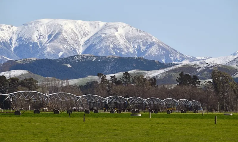 snowy mountains with big irrigators in a field in the foreground