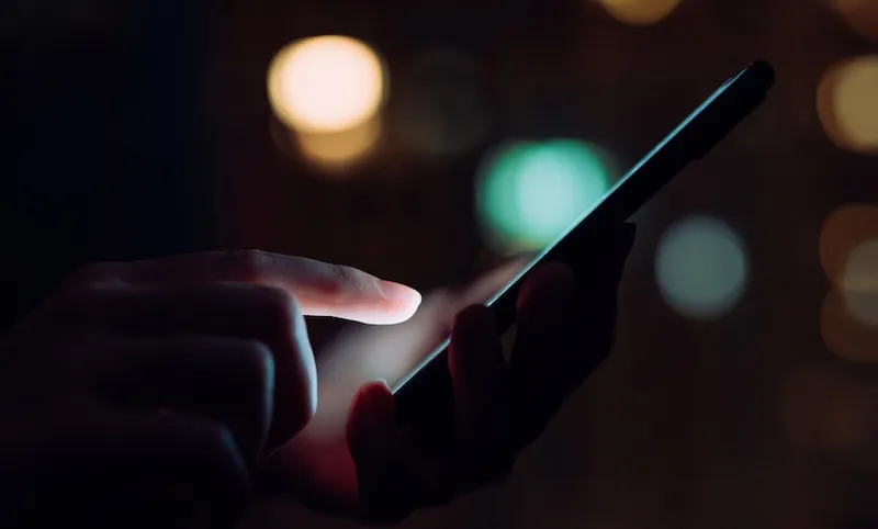Close up of woman's hand using smartphone in the dark, against illuminated city light bokeh