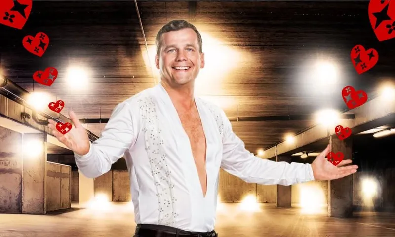 bright lights in the background, a man with lots of fake tan holds his arms wide while wearing a white shirt with a deep v cut to his bellybutton, and a slightly unsettling look in his eyes
