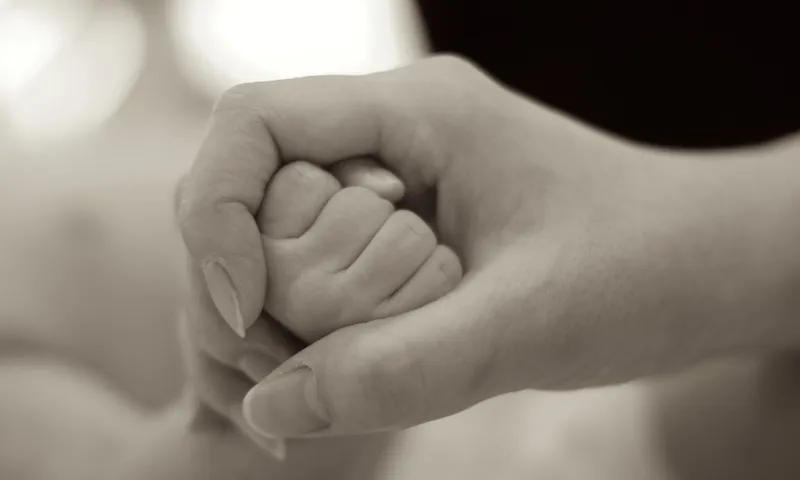 black and white image of adult holding a babies hand