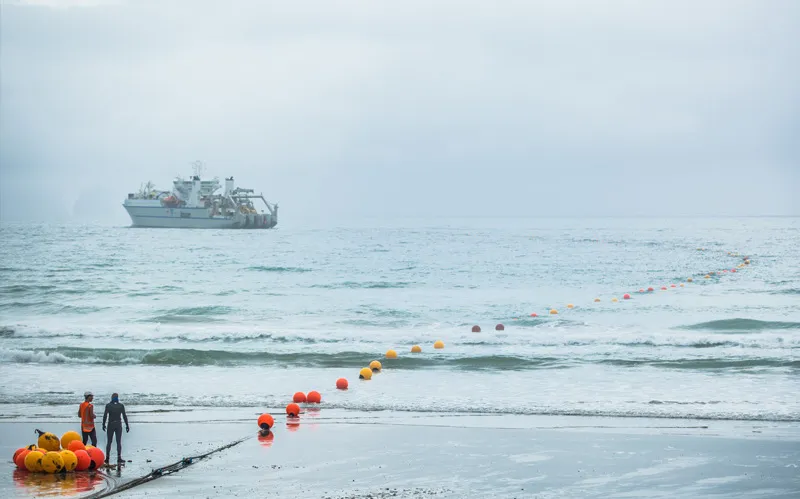 an ocean with some bobbing buoys and a boat and a line whic his the undersea cable