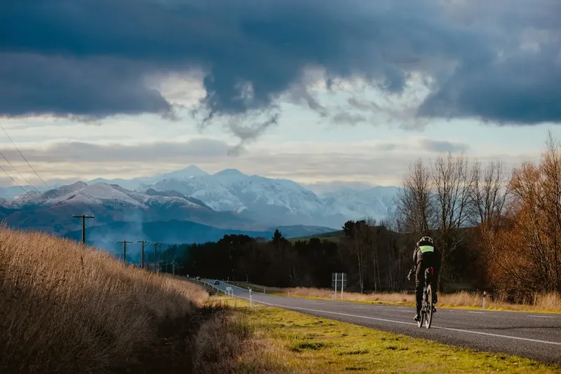 big south island mountains and a long gray road, with wilcox on a bike in a neon vest in the centre of the frame