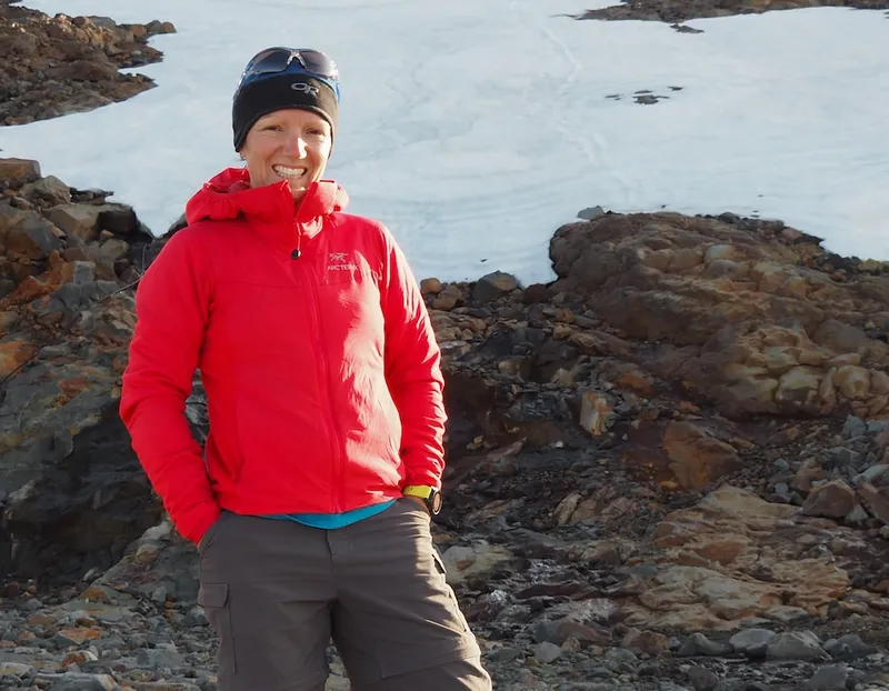 a woman in a red jacket with a patch of snow in the background
