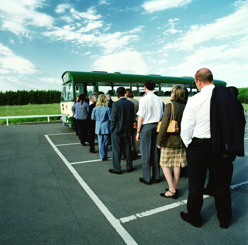 Queue of people waiting to board bus in car park, rear view