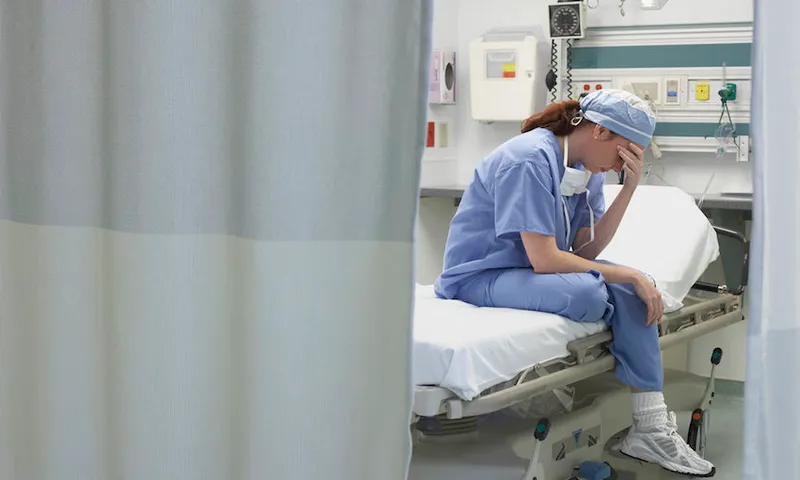 View through privacy curtains to female doctor sitting with head in hand