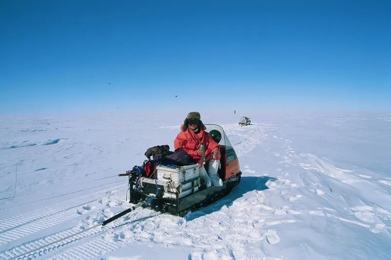endlessly blue sky and that impossible gleaming horizon. in the centre of the frame, a scientist in a red coat cups a mug in his hands. it is very sunny, very empty, very cold