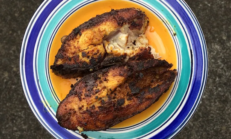 two fried fish fillets sit atop a round plate that is blue, teal and yellow in colour