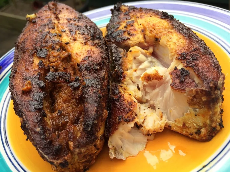 two fried fish fillets sit atop a round plate that is blue, teal and yellow in colour
