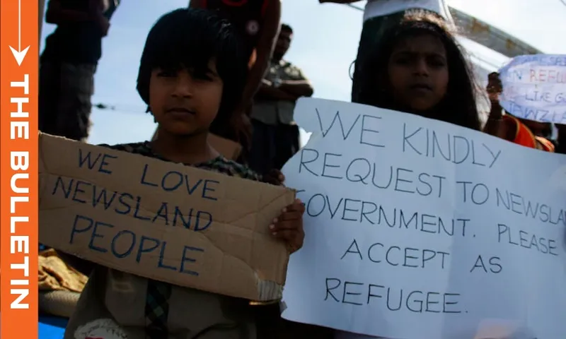 The image shows two Sri Lankan children who are asylum seekers hold signs and pleading for assistance from the New Zealand onboard the MV Alicia in 2011