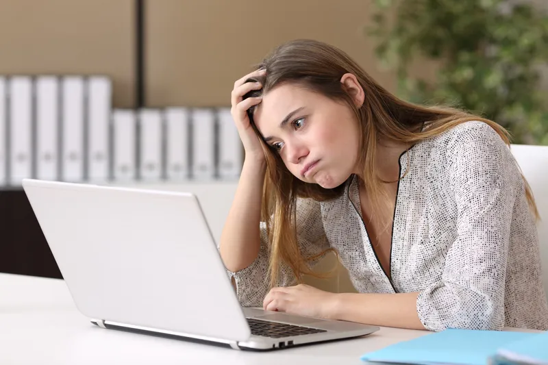 white woman frowns at a bland laptop with some plants, looking frustrated and concerned