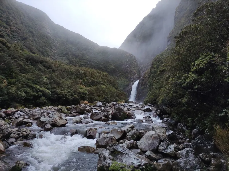 misty mountains and a stream with slippery rocks and steep bushy hills rising into the sky