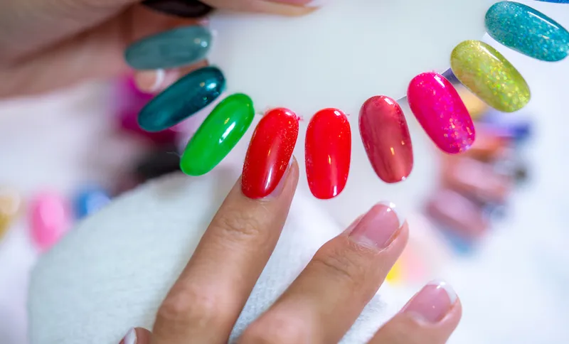 Client choosing color of nail polish for manicure from palette colors. Close up, only hands on white table visible. Nail art, hands care, beauty concept.