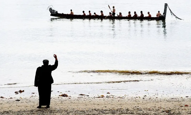 beach with a waka full of people in the grey-toned water