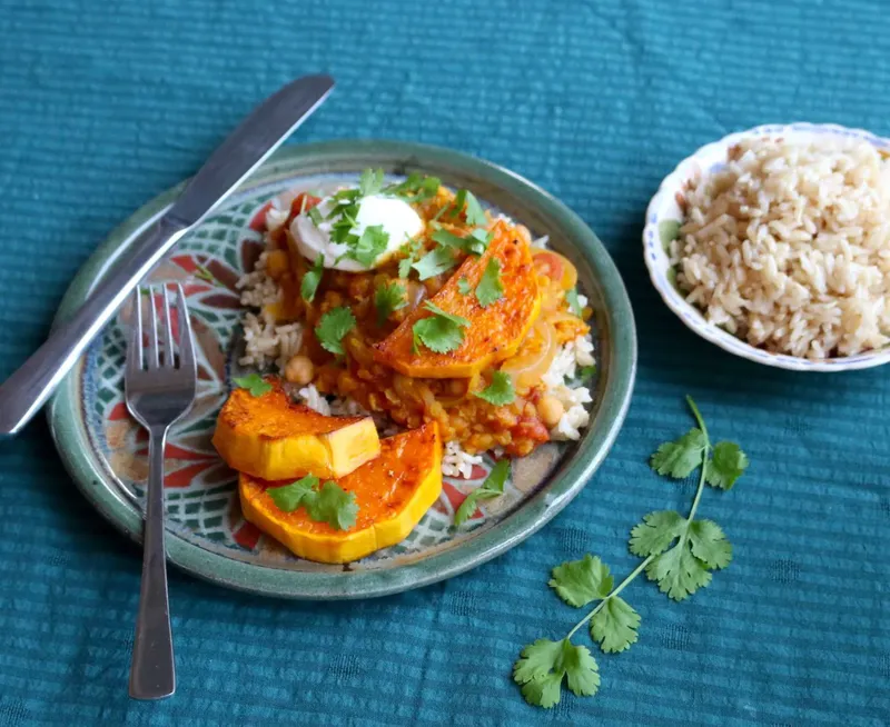 Pumpkin and lentil curry. Served with rice on a mosaic design plate on a blue tablecloth.