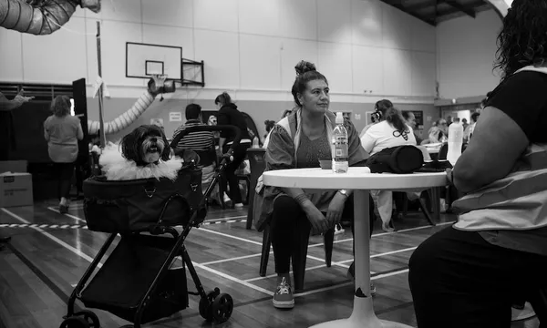 Black and white image of a woman sitting at a table and a dog sitting in a pram next to her
