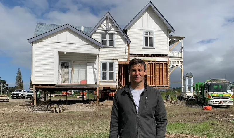 A man stands in front of an old two storey house