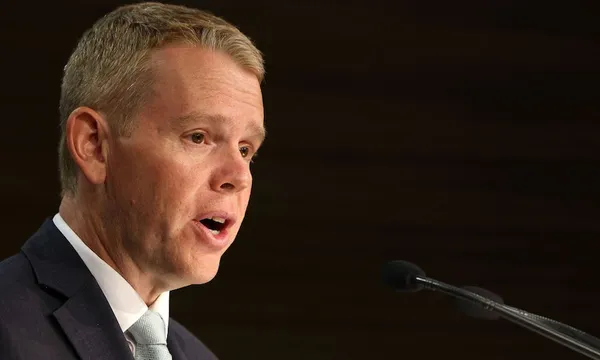 a white man wearing a light teal tie speaking with his mouth open against a black background