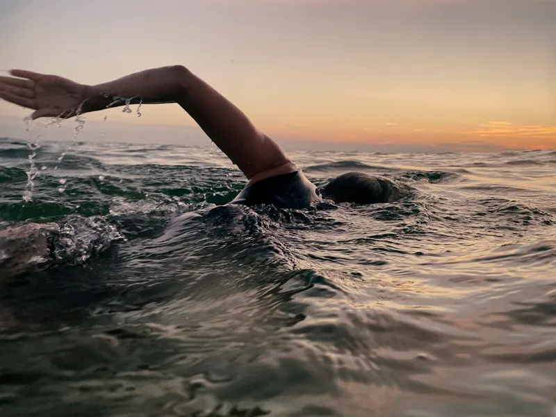 sunset and still water, a person's arm pushing them through the sea