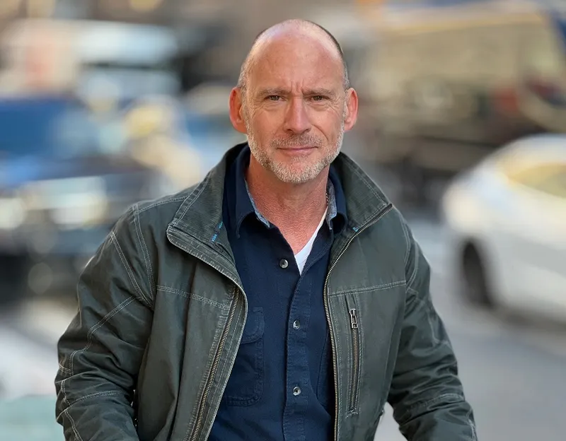 bald white man with out of focus city in background, and a very cool green leather jacket