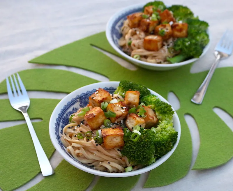 Two bowls of peanut noodles topped with golden tofu and florets of broccoli.
