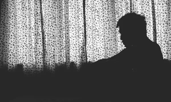 Silhouette Man Sitting By Window At Home