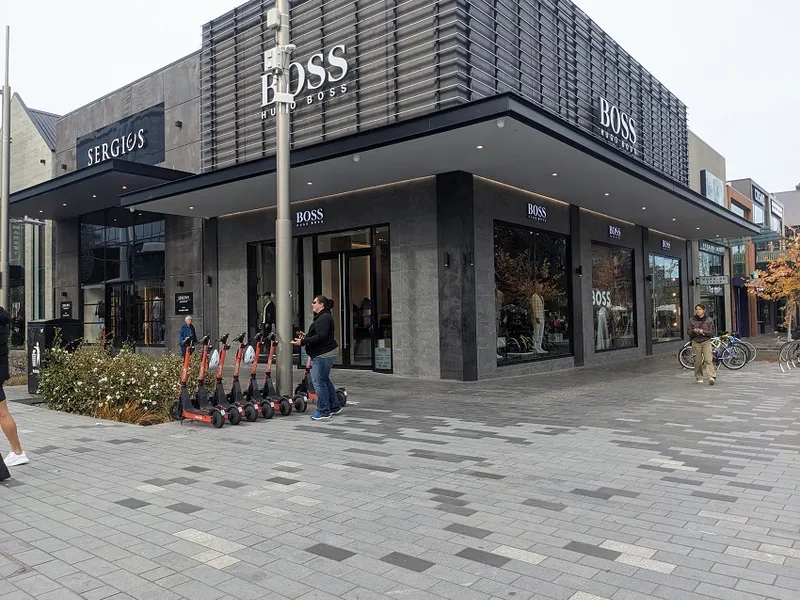 the grey mosaic of tiles with a black office/retail building behind and some very neatly parked orange neon Neron scooters