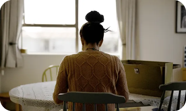 A woman with her hair in a bun sits at a table, back to the camera