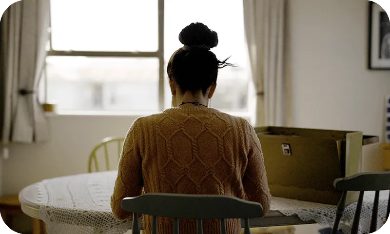 A woman with her hair in a bun sits at a table, back to the camera