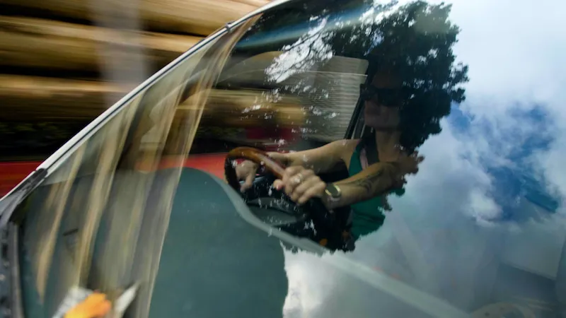 looking through the windscreen at a woman driving a car, with a tree reflected