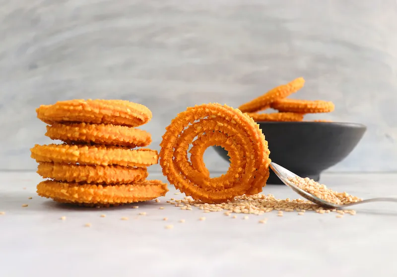 Crunchy fried homemade Chakli in a bowl with sesame seeds. Chakli is a savory snack from India made out of rice, mixed yellow and green lentils along with spices. Mostly eaten during Diwali festival