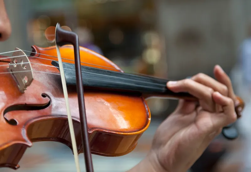 a man's hand is seen holding a violin as the bow is drawn across, the background is blurred