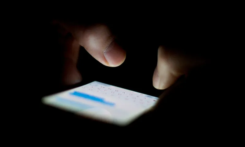 Cropped Hands Typing On Mobile Phone In Dark