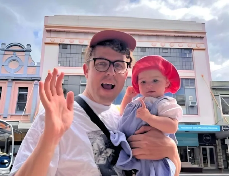 a pakeha man and baby on an auckland street looking happy and waving on a sunny day