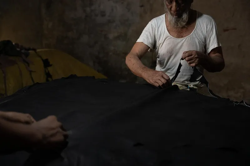 a dark background with hands workingon fabric, perhaps leather.