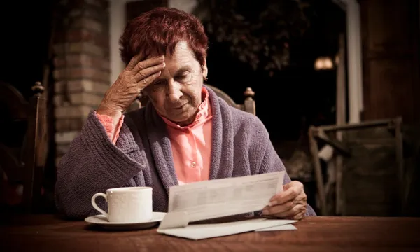 A woman looking tiredly at a letter bill looking exhausted with a cup of tea