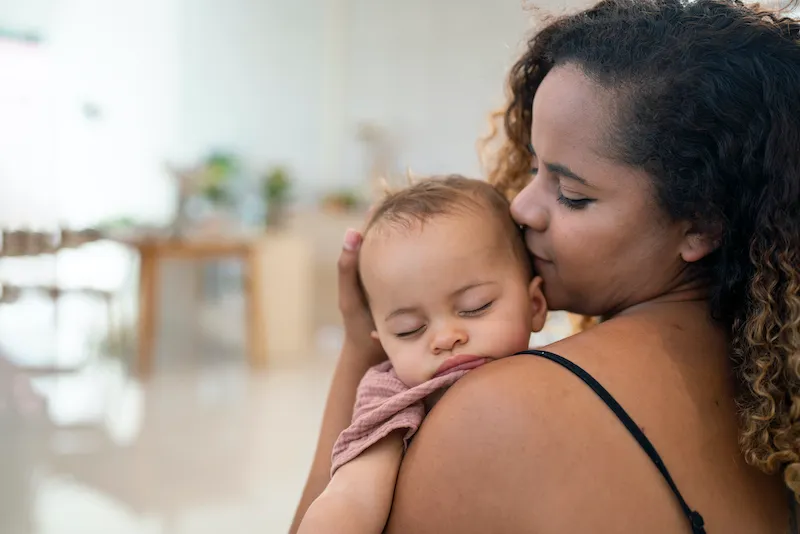 Close Up Of Mother Cuddling Sleeping Baby Daughter At Home