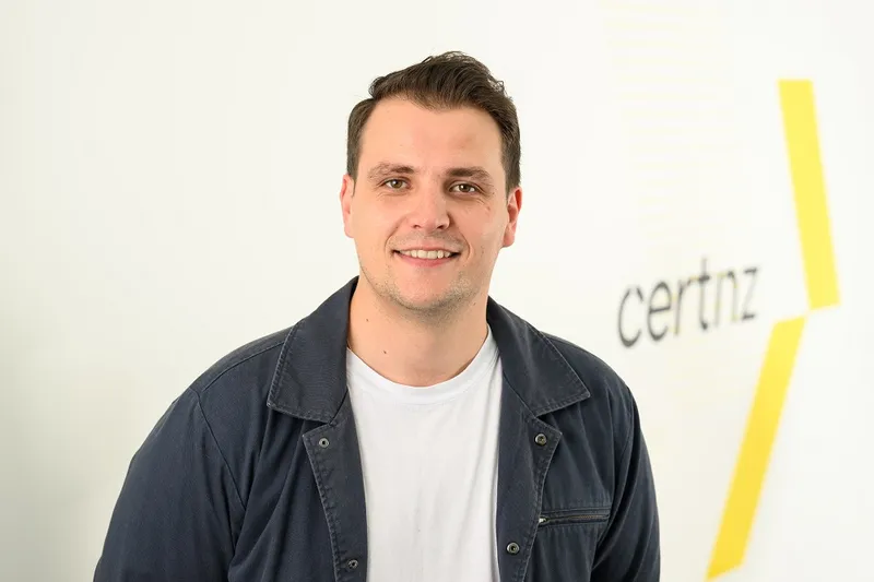 youngish man with pale skin, short brown hair, a blue jacket open to a white tshirt