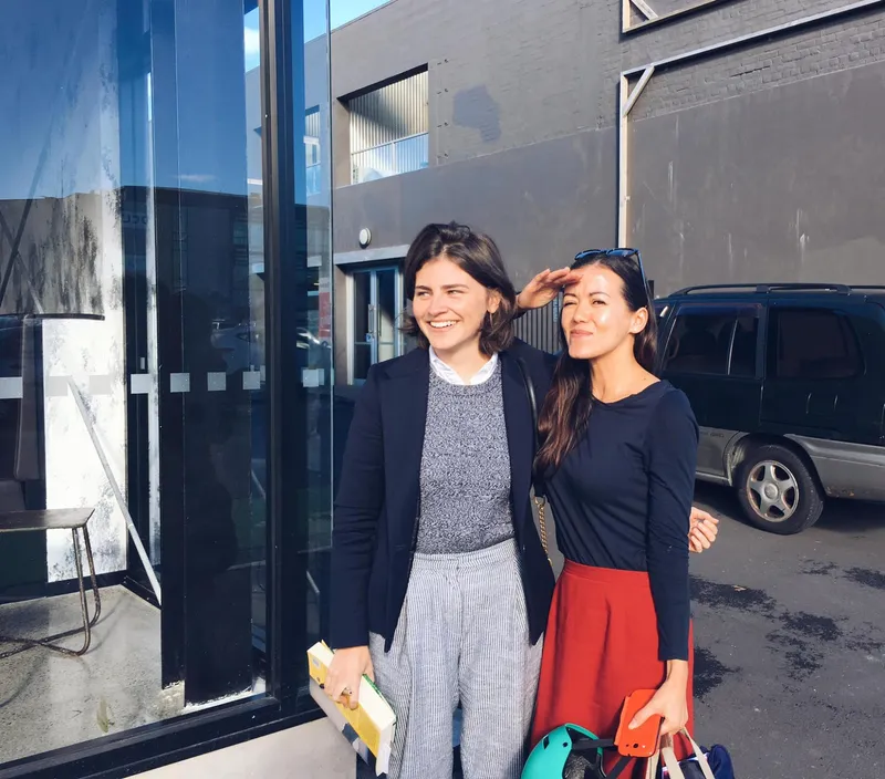 two women standing together in the sunshine, one is light skinned with brown hair and one is brown skinned and petite with black hair