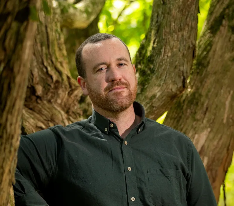 a man in a green shirt with a tree in the background
