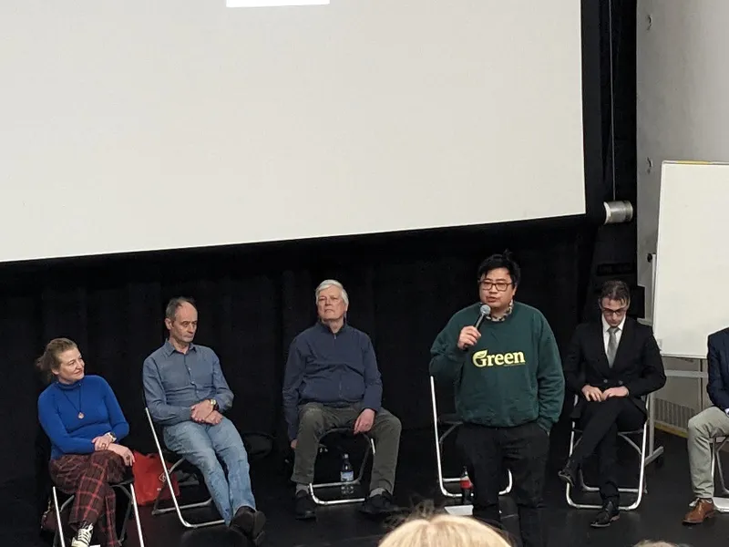 a man in a Green sweater in front of five other people, seated