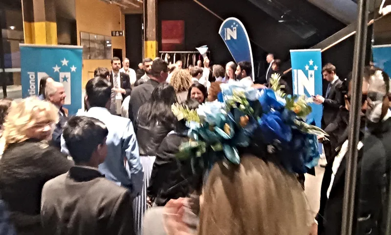 a big crowd of people in what looks like a hall with some national signs in the background