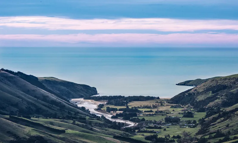 a blue sky and a the visa of a valey with a tangle of mist caught in pine trees and some houses and veilds and the wide wide blue expanse of the ocean
