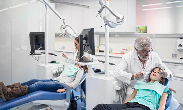 a dental clinic with a child in a chair with their mouth open so a dentist can look inside