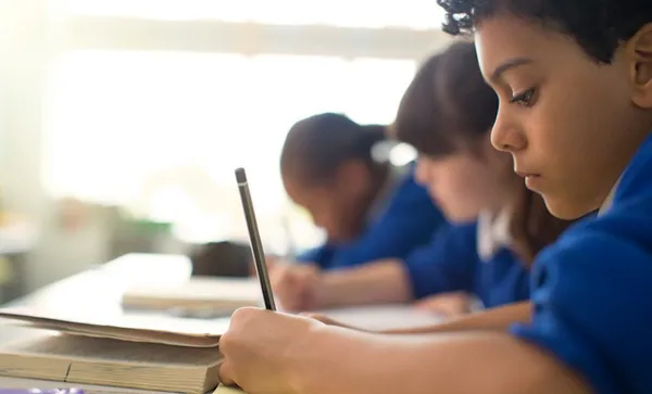 Pupils writing in notebooks at desks in classroom