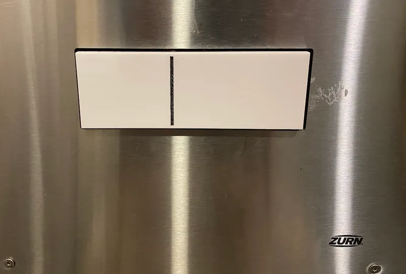 A toilet flush button clearly demarcated between full and partial flushes.