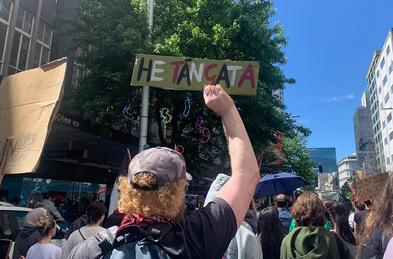 Protestor holds hand painted sign saying "He tāngata"