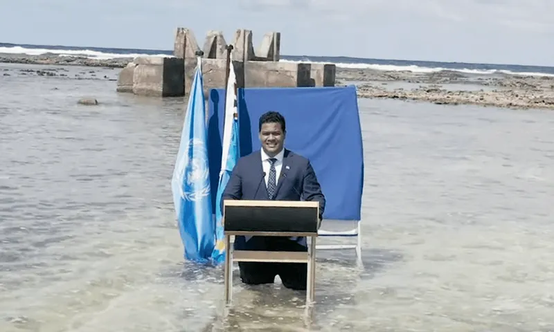 a man in a suit standing in clear tropical seas at a lectern delivering a UN address